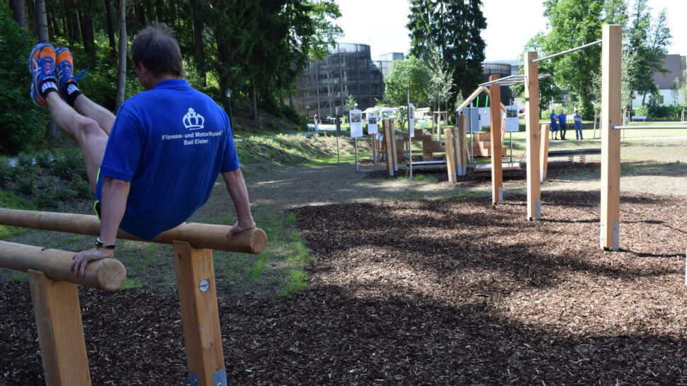 Ein Mann stützt sich mit den Händen an einem Barren ab und hebt die Beine hoch