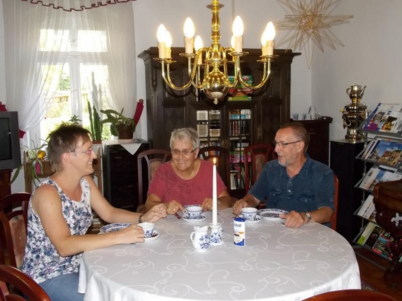 Drei Personen sitzen freudig an einem Tisch und trinken Kaffee
