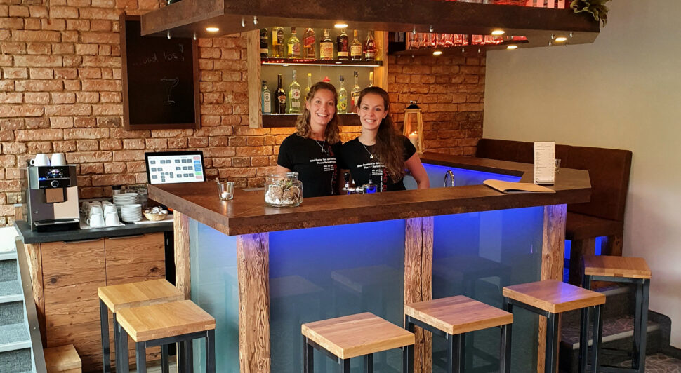 Zwei lächelnde Mitarbeiterinnen hinter der Bar