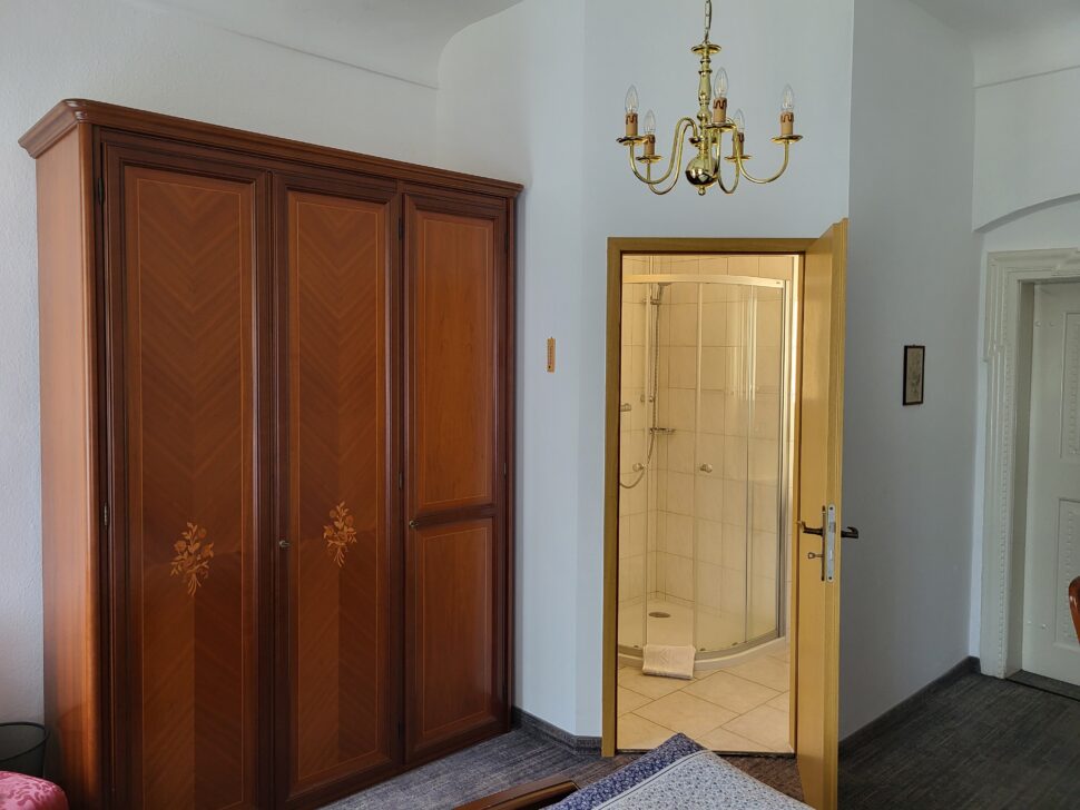 Zimmer mit Holzschrank und Blick in das Badezimmer mit Dusche