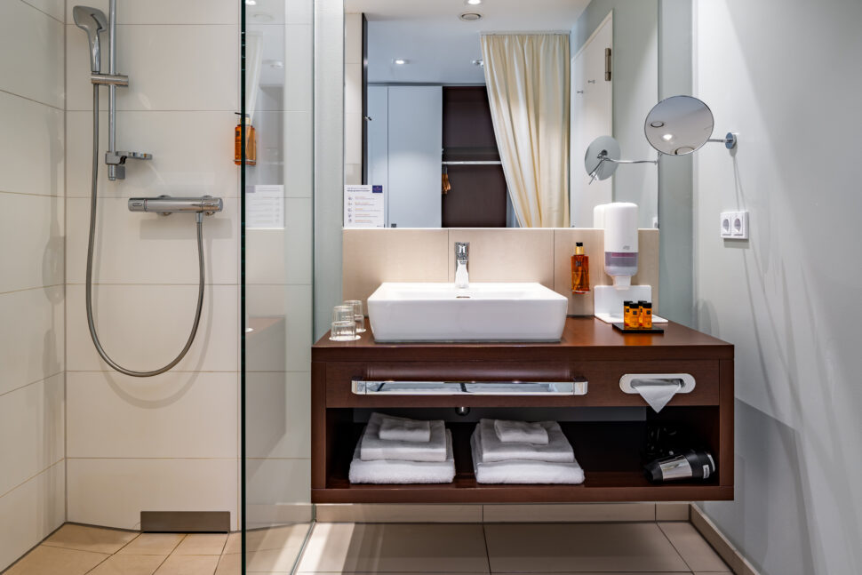 Ein Blick ins Badezimmer: links die Dusche, rechts ein Waschbecken mit Spiegel