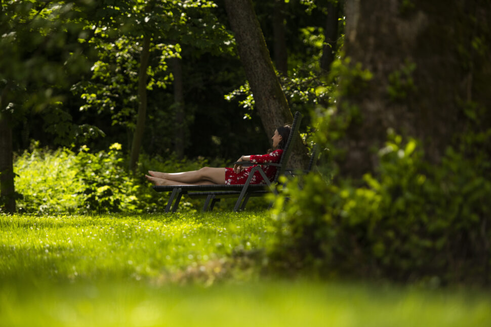 Eine Frau auf einer Liege in einer grünen Wiese mit Bäumen umgeben