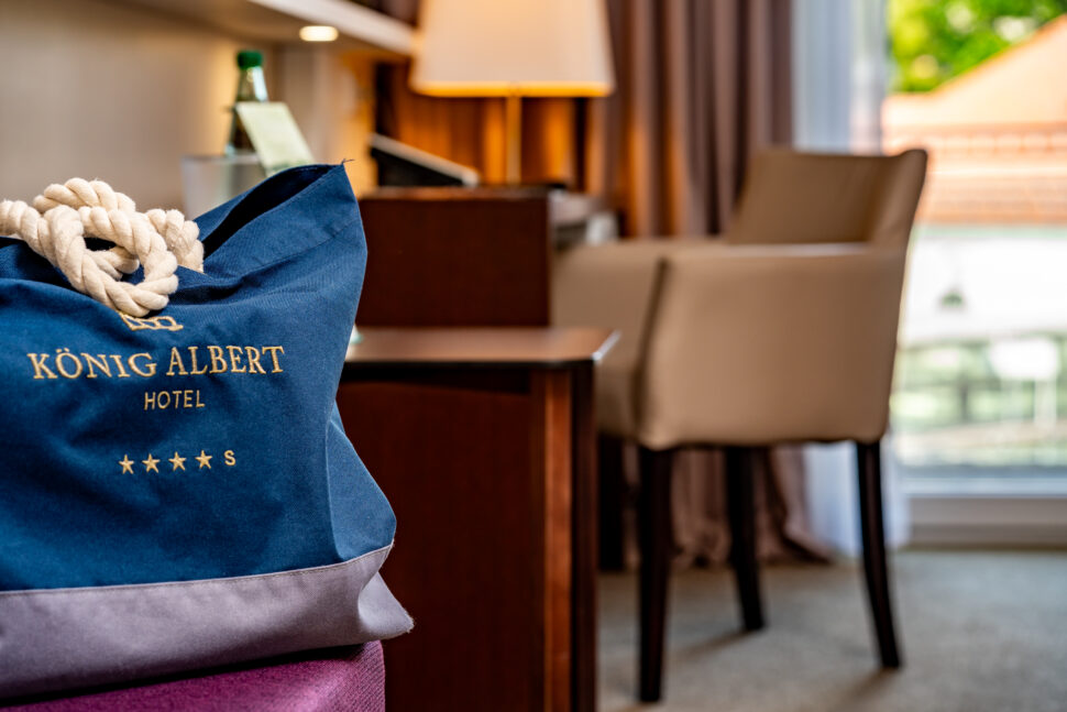 Eine blaue König Albert Hotel Tasche steht im Vordergrund, im Hintergrund ist ein unscharfer Schreibtisch zu sehen