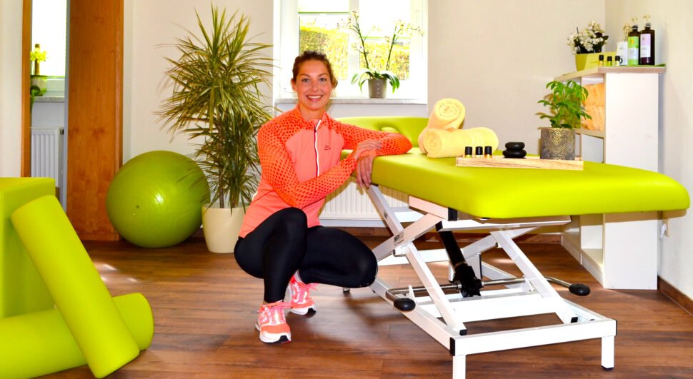 Eine Therapeutin kniet lächelnd neben einer Behandlungsliege